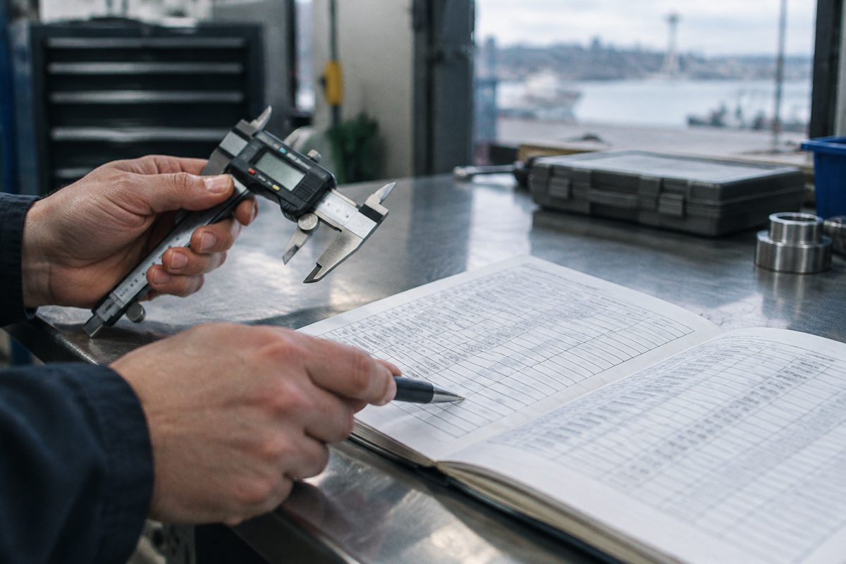 An auditor matches a caliper against its line in a printed calibration register